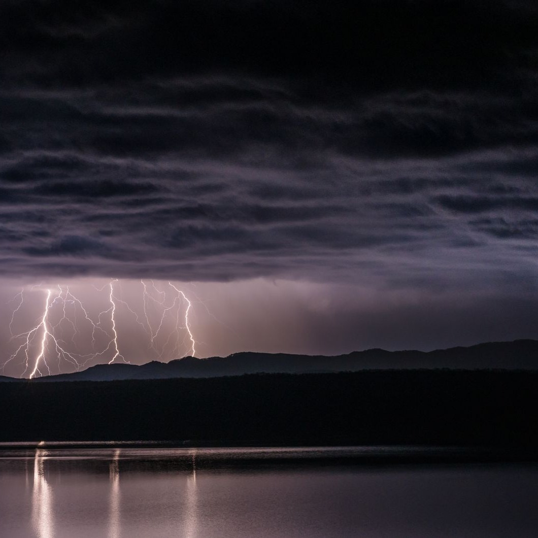 Cover art for Catastrophic: a nighttime lightning storm over mountains, bolts reflected in a lake